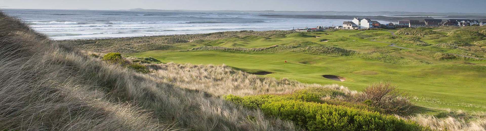 Golf course green with sand traps and clubhouse in distance